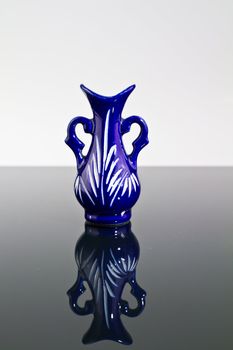 A blue empty vase on a mirror with dark and bright background