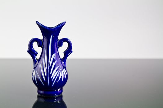 A blue empty vase on a mirror with dark and bright background