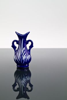 A blue empty vase on a mirror with dark and bright background and mirror image in portrait orientation