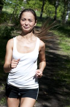 young woman jogging in the park in summer, trees and grass background