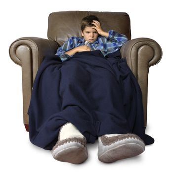 Sick child with thermometer, sitting in a big leather chair covered with blankets.
