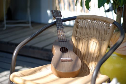 A small wooden guitar resting on a wicker and metal chair.