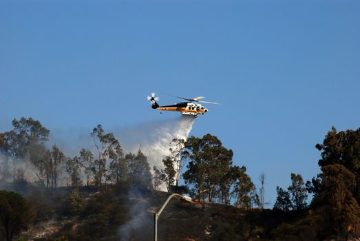 A helicopter from the Los Angeles County Fire Department drops water on a wildfire above Griffith Park, California.  August 2008