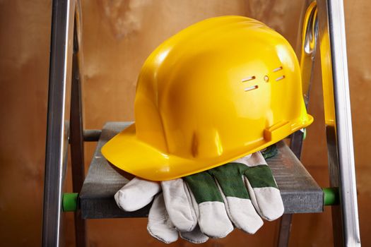 yellow helmet and working gloves on stepladder, selective focus on nearest parts