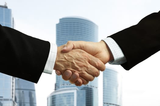 Hand shake of businessmen on corporate building background, focus point on center