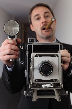 Photo of a retro 1940's style photographer taking a photo with an old 4x6 camera.  Photographer out of focus and camera in focus.