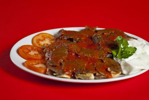 Traditional turkish iskender kebab served on white plate with vegetables mix