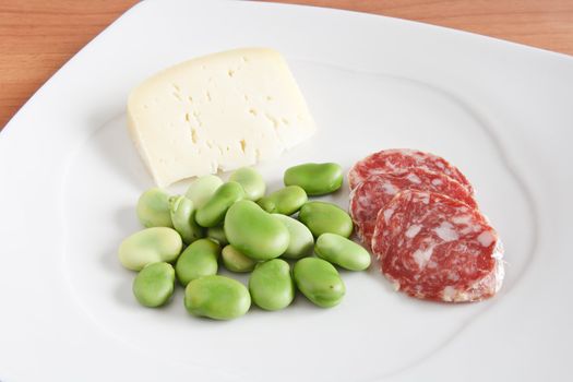broad beans with pecorino cheese and salami slices on a white plate