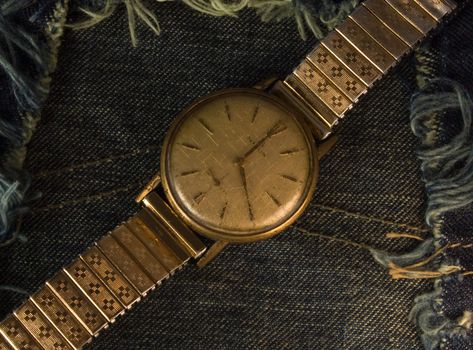 Retro golden wristwatch close up over blue jean cloth background.