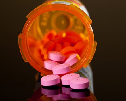 Set of round purple tablets pouring from an orange pill bottle