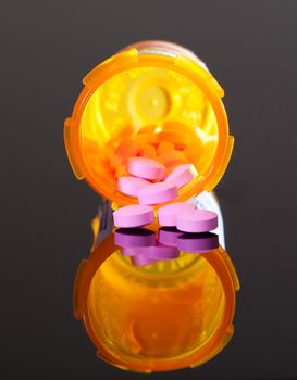 Set of round purple tablets pouring from an orange pill bottle