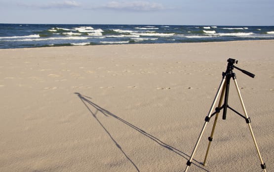 Camera tripod standing in the seasand. Sea sand and waves background.