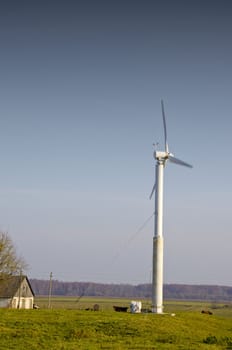 Windmill in the countryside. Farm building and the cows grazing around.