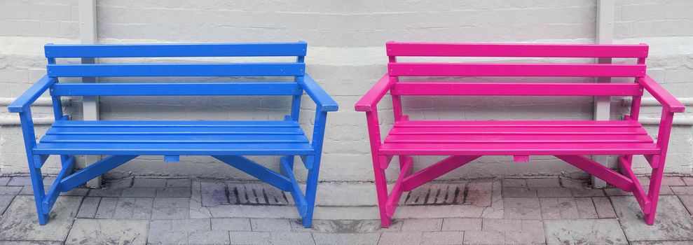 A blue and a pink bench in front of a white wall