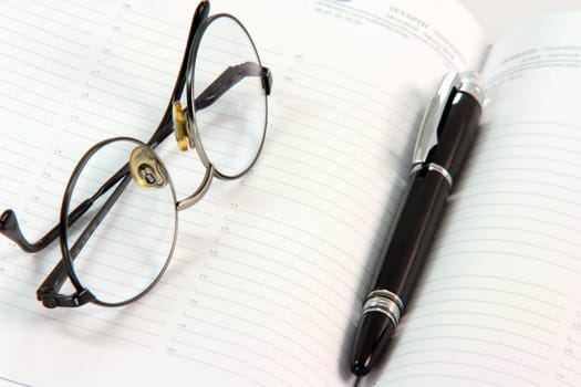 spectacles with black ball pen on open diary business concepts