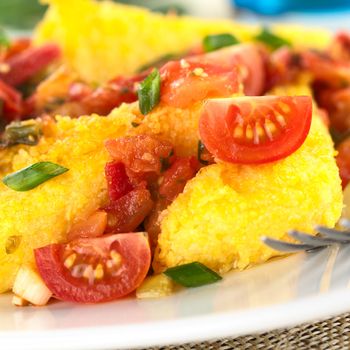 Polenta slices with Hogao, also called Criollo Sauce, which is a Colombian sauce made of tomato, onion and cilantro (Selective Focus, Focus on the upper edge of the right tomato slice and the front of the tomato pieces beside)