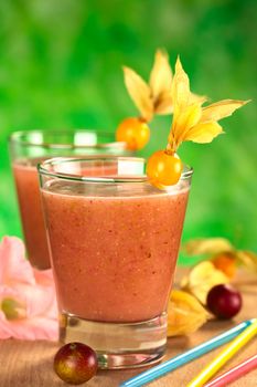 Juice out of Camu camu berry fruits (lat. Myrciaria dubia) which are grown in the Amazon region and have a very high Vitamin C content (Selective Focus, Focus on the front rim of the glass and the physalis berry garnish)