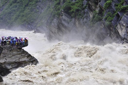 Tourists on a viewing platform looking out over the wild river at Tiger Leaping Gorge in Yunnan, China