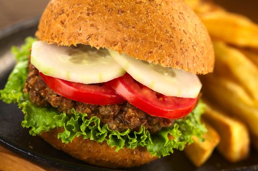 Vegetarian lentil burger in wholewheat bun with lettuce, tomato and cucumber accompanied by French fries (Selective Focus, Focus on the front of the lettuce, lentil burger, tomato and cucumber) 