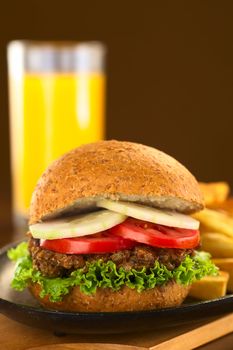 Vegetarian lentil burger in wholewheat bun with lettuce, tomato and cucumber accompanied by French fries and orange juice (Selective Focus, Focus on the front of the sandwich) 