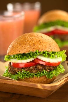 Vegetarian lentil burgers in wholewheat bun with lettuce, tomato and cucumber accompanied by camu camu juice (Selective Focus, Focus on the front of the sandwich) 