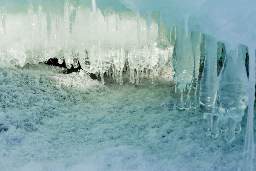 Ice and icicles forming a cave-like structure beautifully illuminated by sunlight.