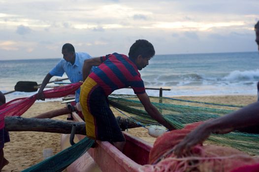 Hikkaduwa, Sri Lanka - February 21, 2011: Group of Sri Lankan fishermen packing fishing net. Fishing in Sri Lanka is a tough job but this is the way they earn their living