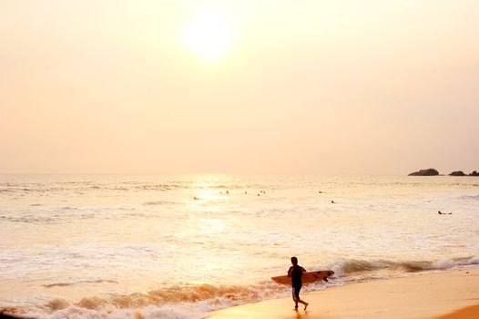 Hikkaduwa, Sri Lanka - March 08, 2011: Surfer on the ocean beach at sunset in Hikkaduwa. Hikkaduva - is the second best surf paradise in Sri Lanka 