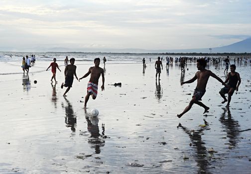 Bali, Indonesia - April 4, 2011: People plaing soccer on the  Kuta beach.Kuta's six-kilometer-long, crescent-shaped surfing beach, protected by a coral reef at its southern end, and long and wide enough for Frisbee contests and soccer games, is famous for its beautiful tropical sunsets