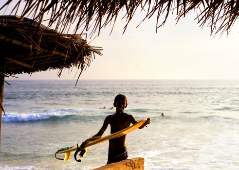 Hikkaduwa, Sri Lanka - January 23, 2011: Portrait of young local surfer with surfboard in front of the ocean