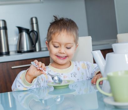 Happy little cute boy in pajamas eating breakfast at a table in the kitchen