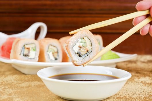 hand holding sushi with chopsticks at table