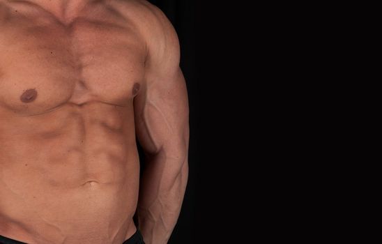 Muscular male torso of bodybuilder on black background