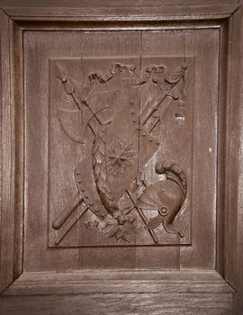 Brown wooden carved palace door with a coat of arms. The helmet shield depict swords.