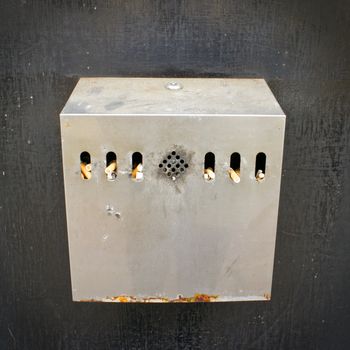 A metal cigarette disposal bin with many cigarette ends
