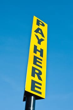 A yellow pay here sign against a vibrant blue sky