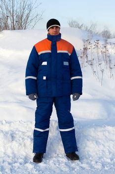 Worker in the winter suit consisting of a jacket and trousers against the backdrop of the snow