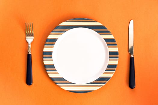 Nice image of a plate with a knife and fork on orange surface