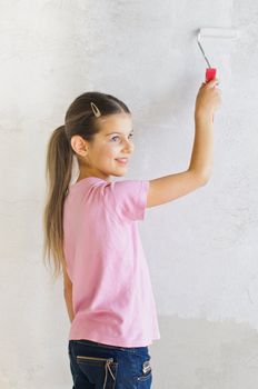 Happy beautiful girl painting a wall with roller