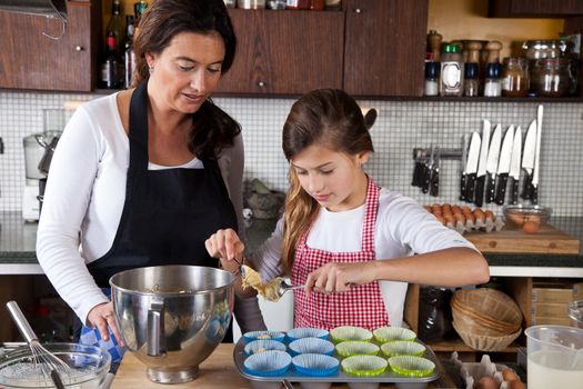Mother is helping daughter making cupcakes in the kitchen