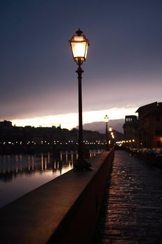 Night in Florence. Glowing vintage street lamp on background with Arno river