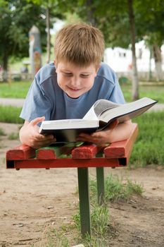 schoolboy reads the book on a bench in park
