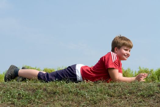 little boy lays on a grass with sky at background 