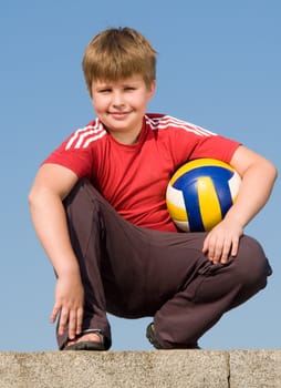 sitting boy with volleyball ball on a blue sky