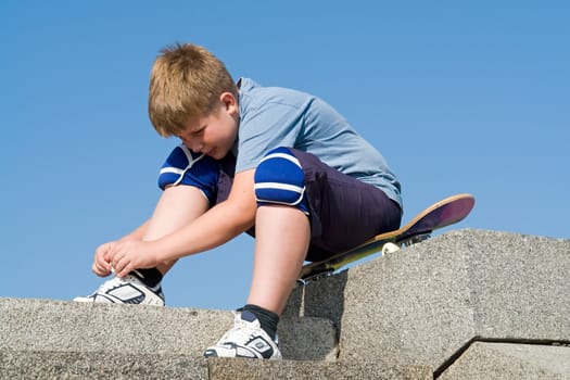 boy ties the shoe-lace sitting on the skateboard