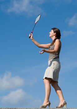 young woman playing badminton on a blue sky