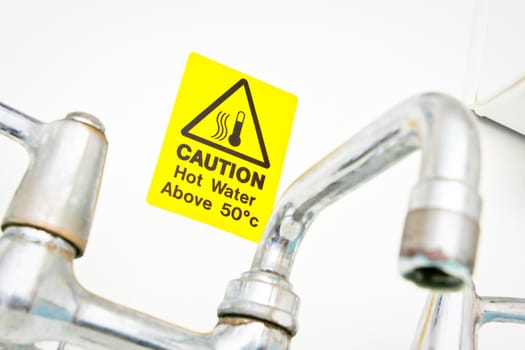 A bright yellow hot water warning notice behind a chrome tap