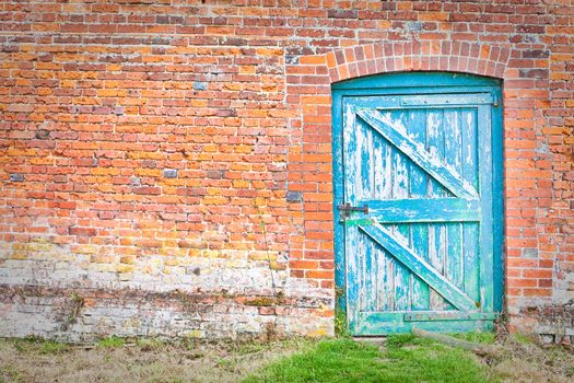 A quirky blue door set at an odd angle in a red brick wall in an English country garden