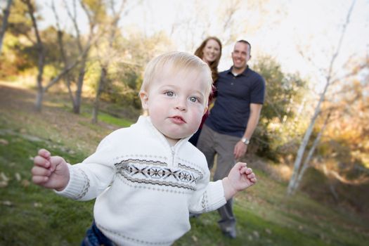 Cute Young Boy Walking in the park as Parents Look On From Behind.