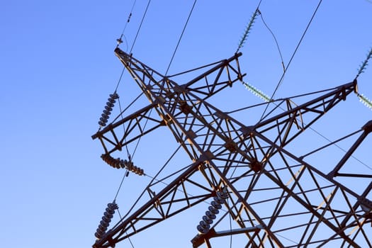 Fragment of electrical high-voltage metal pillar against the background of blue sky